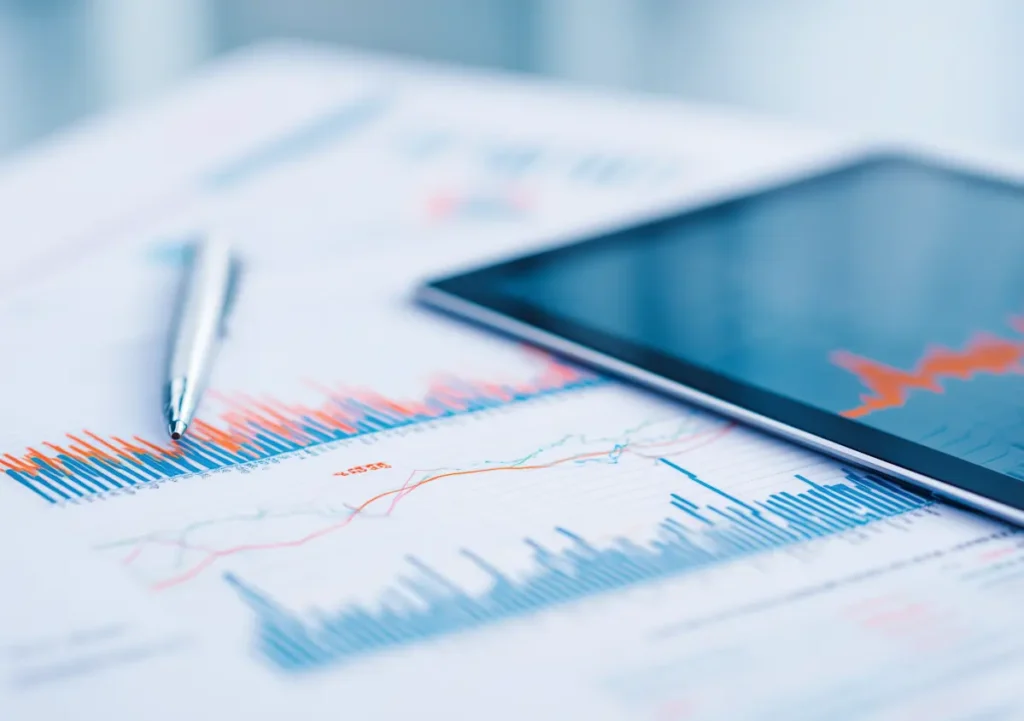 Relatórios financeiros com gráficos de barras e linhas, acompanhados por uma caneta e um tablet com dados em ecrã, representando análise de dados financeiros