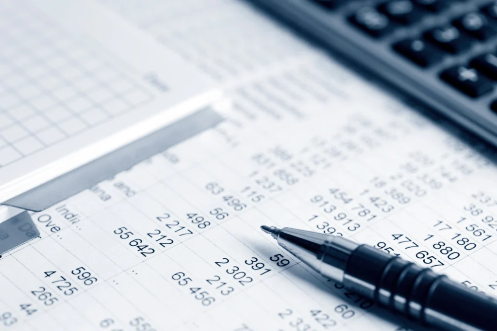 Folha de cálculo com dados financeiros e caneta, usada em contabilidade e análise de contas empresariais.