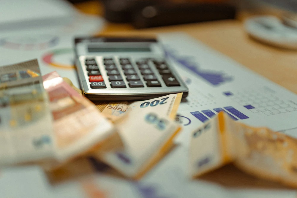 Notas de euro, calculadora e relatórios financeiros utilizados no planeamento financeiro e controlo de custos empresariais.